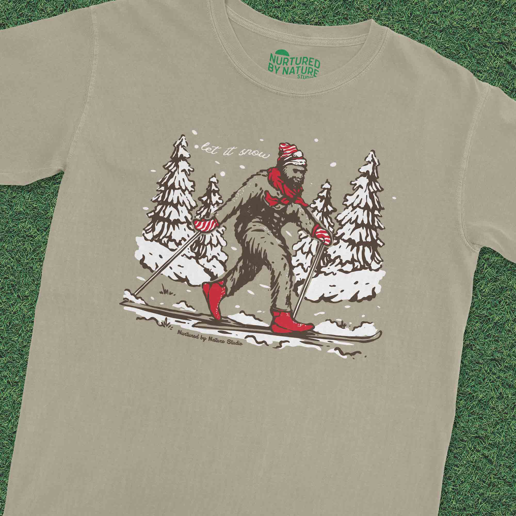 products/Bigfoot-Skiing-in-the-Snow-Nurtured-by-Nature-Studio-Graphic-T-Shirt-on-grass.jpg